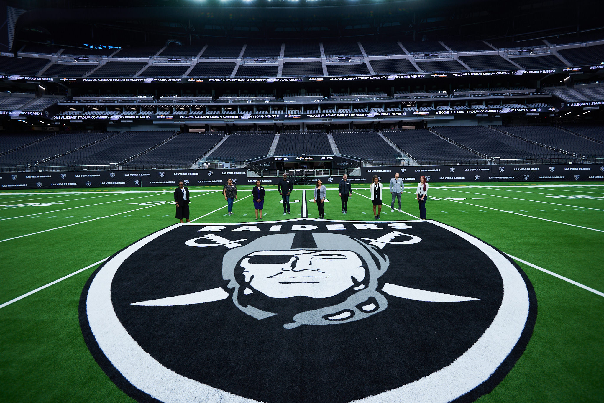 Nine Allegiant Stadium Community Advisory Board members standing in the Raider’s field in Las Vegas, NV